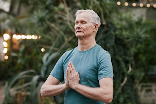 An elderly man meditating surrounded by plants and fresh air. An aging gentleman working on his mental clarity with meditation.