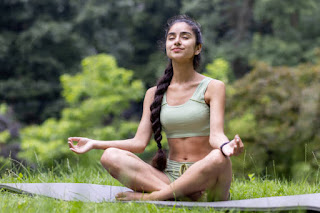 A young woman meditating in a cross-legged position in nature, promoting relaxation and deep breathing