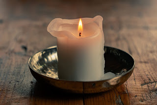 A white candle lit with running wax. Captured during golden hour in a beautiful metal candle holder