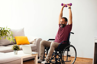 Man in a wheelchair lifting dumbbells in a living room, showing how adaptive yoga and fitness can be incorporated into daily life.