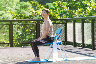 Woman seated on a chair practicing yoga on a wooden deck, illustrating Seated Mountain Pose in adaptive yoga for beginners.