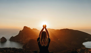 A woman standing on a mountain at sunrise, hands raised, symbolizing the awakening and clarity achieved through meditation.