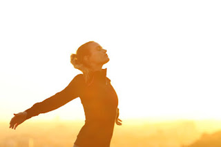 A woman stands with arms outstretched, embracing the morning sun and the infinite space around her, capturing the essence of formless meditation and the expansion of consciousness through Jhanas practice.