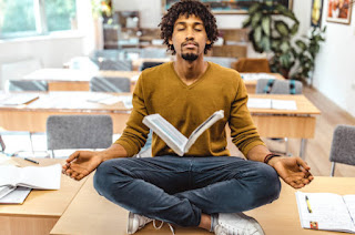 Student sitting cross-legged, meditating with books or a laptop nearby, study environment, focus on relaxation and concentration, indoor setting.