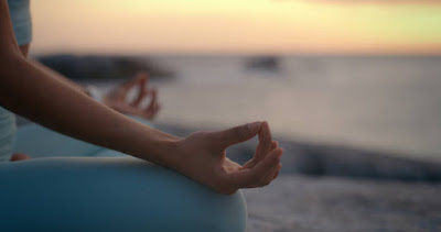 Close-up of hands in a meditation mudra against the backdrop of an ocean at sunset, symbolizing the practice of joy and non-attachment in the first and second Jhanas.