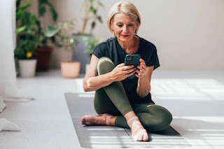 An elderly woman sitting on a yoga mat, and holding a phone, listening to a guided meditation from headspace in a cozy living room.