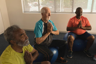 A small group of older adults sitting in a circle at an assisted living facility, meditating together with a facilitator leading the session.