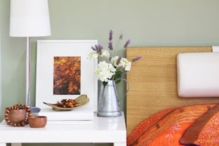 A bottle of lavender essential oil next to a diffuser on a tidy nightstand, with soft lighting in the background.