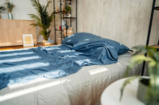 A decluttered bedroom with open windows allowing natural light, wooden furniture, and soft bedding.