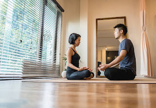 A couple sitting cross-legged on their bed, practicing meditation together in a peaceful bedroom with calming décor.