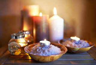 A bedside table with lit candles and a Himalayan salt lamp, casting a warm glow in a tranquil bedroom.