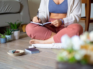 A person sitting with a journal and pen, reflecting on their yoga and meditation practice, with a cozy setting in the background.