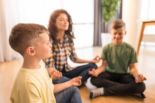 A family, including parents and a teenage child, sitting together in a circle or on a couch with closed eyes, practicing meditation.