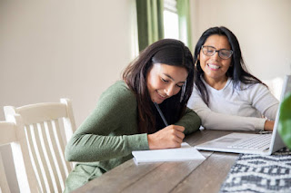 A mother and teenage daughter sitting together with notebooks, reflecting and writing about their day as part of mindfulness practice.