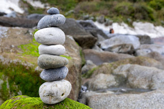 Balanced stones or person in yoga pose near nature, representing stability and balance between personal goals and responsibilities.