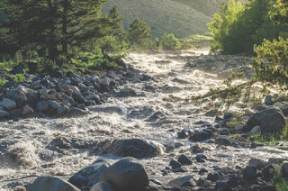 A gently flowing river with clear water winding around rocks, illustrating the concept of adapting to obstacles with grace.