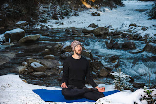 A person meditating by a serene, snow-covered lake in Washington State, surrounded by winter landscapes, embodying the practice of Santosha.