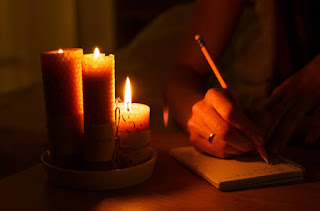 Close-up of hands writing a gratitude list on a journal in Seattle, Washington, accompanied by a warm candle, emphasizing mindful gratitude and Santosha.