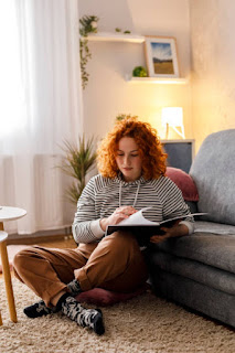 Young woman sitting on the floor with a journal, writing thoughtfully in a cozy living room setting, symbolizing self-reflection and mindfulness.