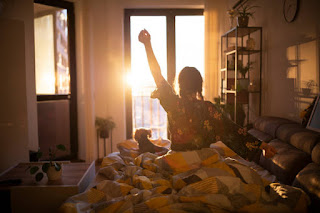 A woman stretching her arms in bed as morning sunlight fills the room, highlighting the importance of light exposure for energy and emotional well-being during winter.