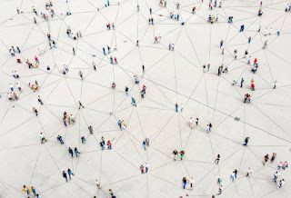A top-down view of a large open space with groups of people connected by lines, symbolizing the interconnected web of humanity.