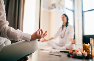 Close-up of a person’s hand in a mudra during meditation, with another practitioner in the background, emphasizing the use of mudras for energy alignment in Kundalini Yoga.