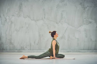 A person in Pigeon Pose folds forward on a mat, with a subtle hourglass in the background showing suspended sand, illustrating how deep stretch yoga slows the perception of time.