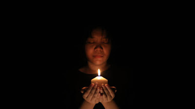 A close-up of a flickering candle flame against a dark background, with faint ripples symbolizing timeless focus. A blurred figure meditates in the distance, practicing Trataka.