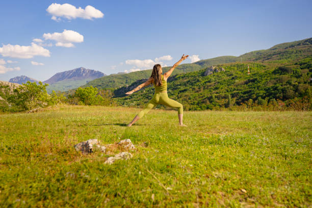 A woman practicing warrior II in a sunlight field, symbolizing grounding and presence.
