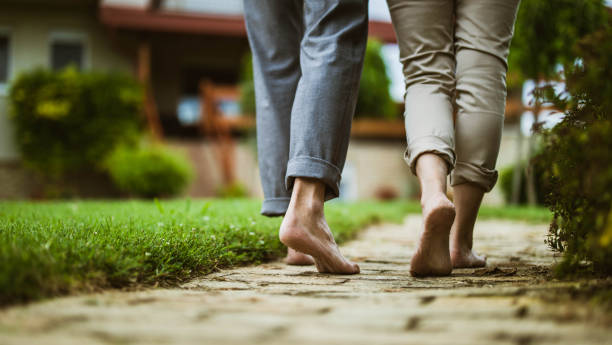 Two people walking barefoot along a garden stone path, symbolizing grounding and mindfulness through silent walking meditation.